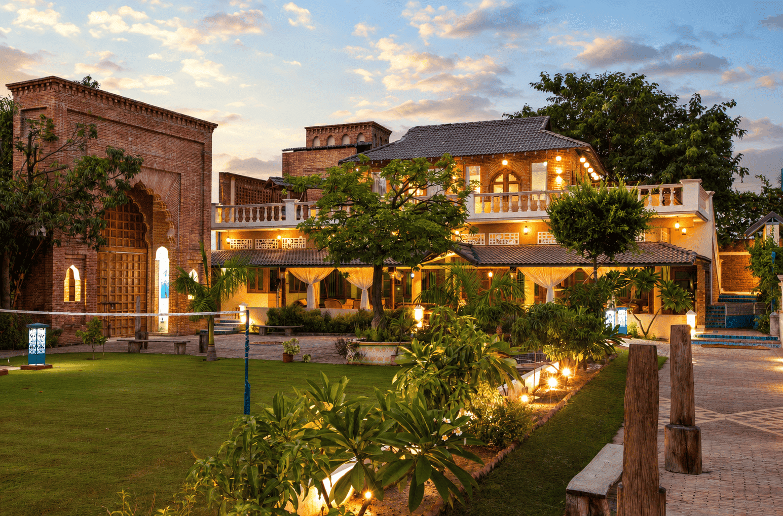 A luxurious brick resort villa with a manicured green lawn, lit up beautifully during a vibrant sunset.