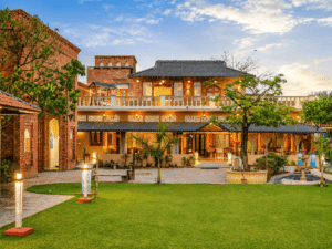 A luxurious brick resort villa with a manicured green lawn, lit up beautifully during a vibrant sunset.